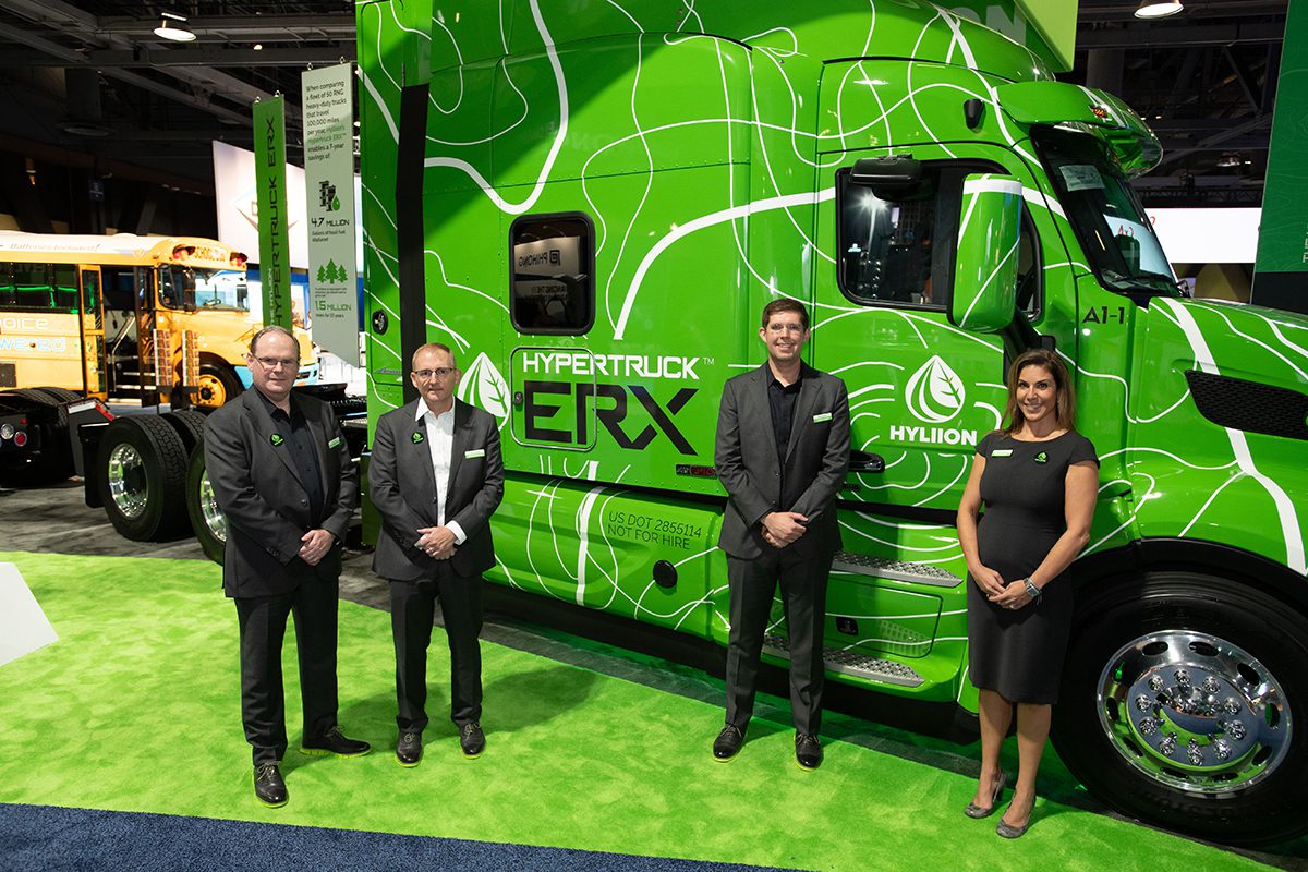 three men and a woman standing in front of green semi truck